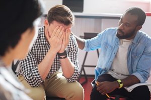 male comforts friend during group therapy